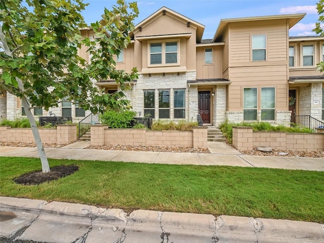 townhome / multi-family property with a front yard and stone siding