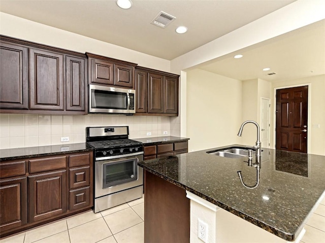 kitchen featuring a sink, dark stone countertops, light tile patterned floors, and stainless steel appliances