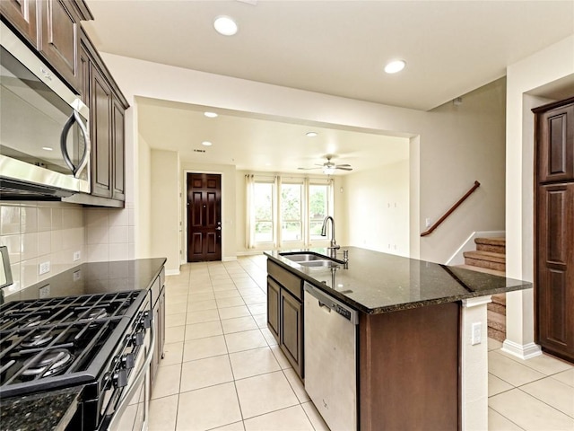 kitchen with backsplash, a sink, light tile patterned floors, dark stone countertops, and stainless steel appliances