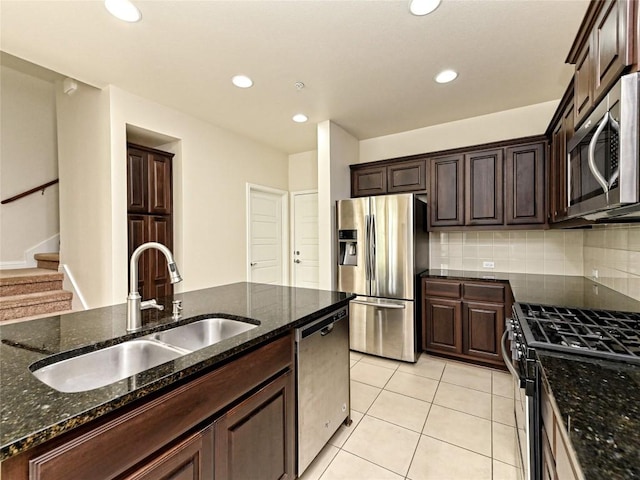 kitchen featuring a sink, dark stone counters, stainless steel appliances, decorative backsplash, and light tile patterned floors