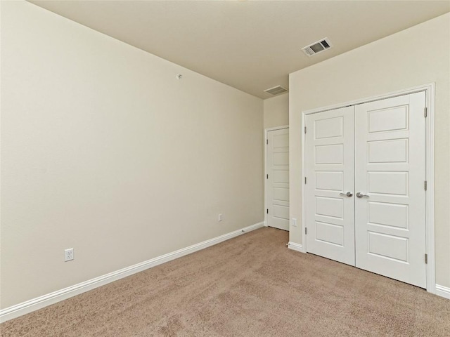 unfurnished bedroom featuring visible vents, baseboards, a closet, and light colored carpet