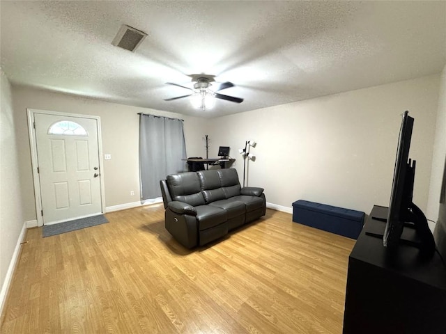 living room with a ceiling fan, a textured ceiling, visible vents, baseboards, and light wood-style floors