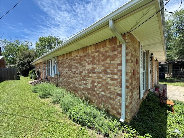 view of side of home featuring a yard, brick siding, and fence