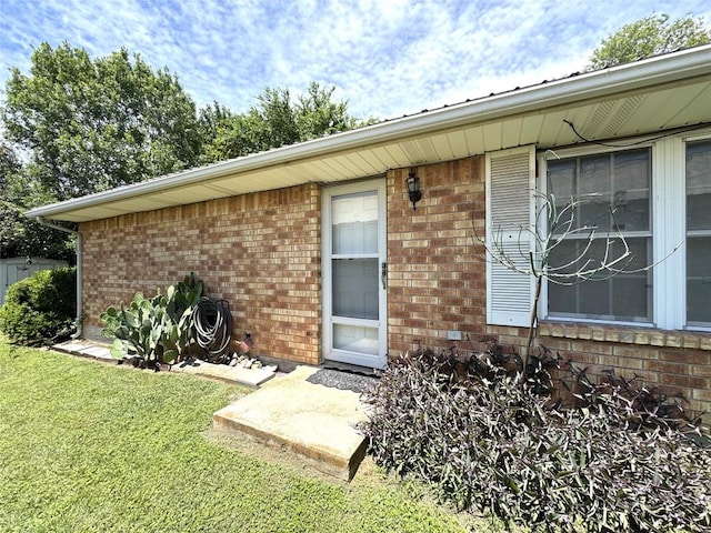 entrance to property featuring a yard and brick siding