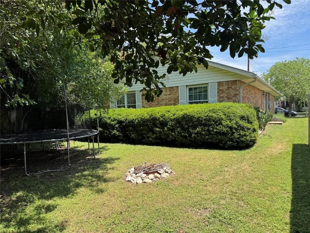 view of side of property featuring brick siding, a trampoline, a fire pit, and a yard