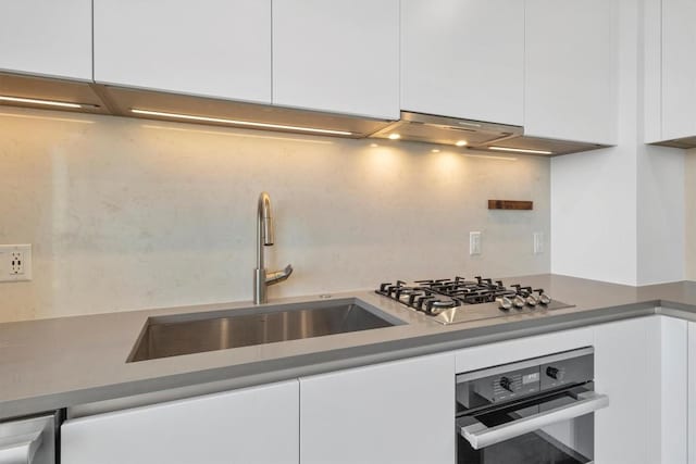 kitchen featuring wall oven, white cabinetry, under cabinet range hood, a sink, and stainless steel gas stovetop