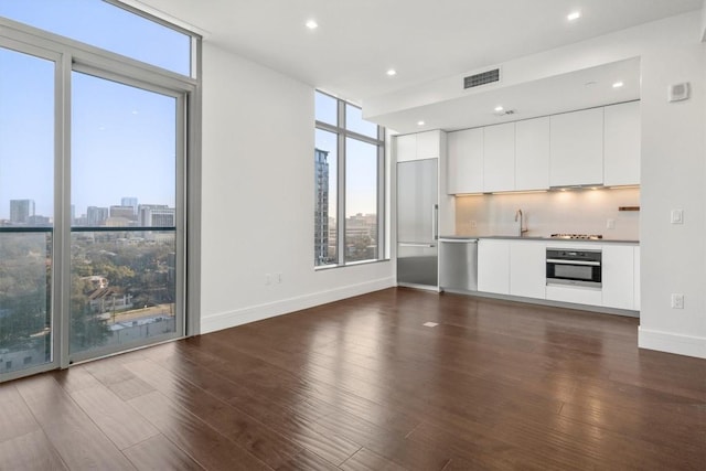 unfurnished living room featuring plenty of natural light, floor to ceiling windows, dark wood-style floors, and visible vents