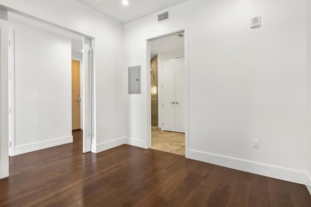 empty room featuring baseboards, electric panel, dark wood-style floors, and visible vents