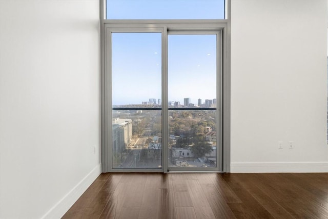 unfurnished room featuring a view of city, baseboards, and wood finished floors