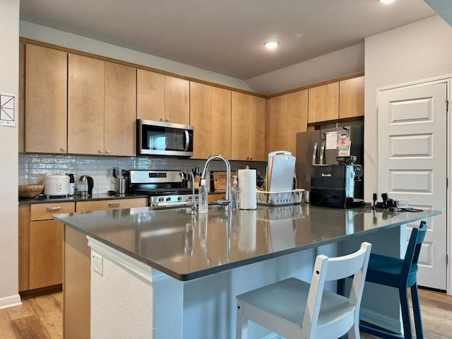 kitchen featuring light wood-style floors, appliances with stainless steel finishes, a breakfast bar area, and dark countertops