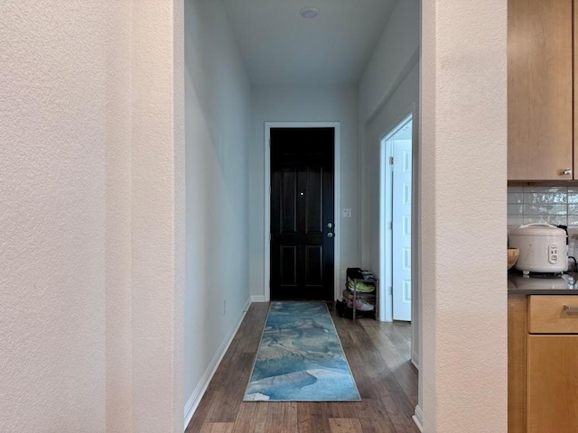 doorway with baseboards, a textured wall, and dark wood-style floors