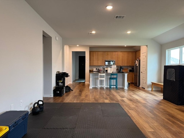 kitchen featuring visible vents, appliances with stainless steel finishes, brown cabinets, dark wood-style floors, and a breakfast bar