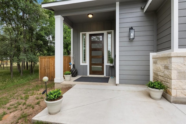 view of exterior entry with fence, covered porch, and board and batten siding