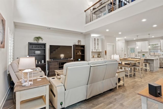 living area featuring light wood-style floors, plenty of natural light, recessed lighting, and a towering ceiling