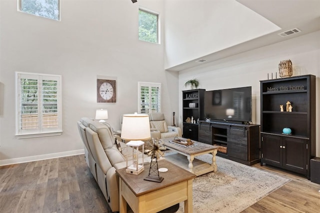 living room with baseboards, a towering ceiling, wood finished floors, and visible vents