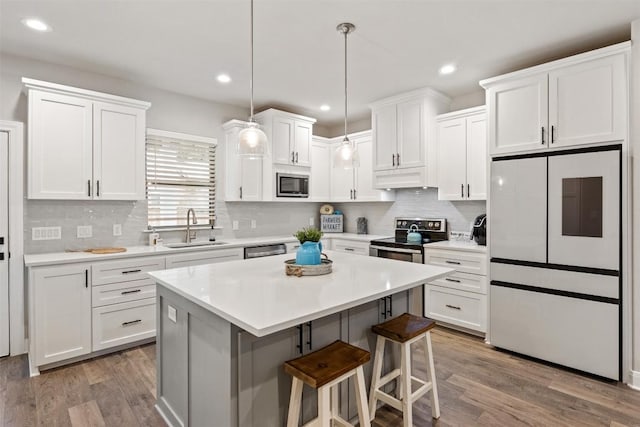 kitchen with a sink, appliances with stainless steel finishes, white cabinets, and wood finished floors