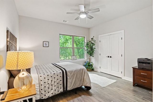 bedroom with a ceiling fan, visible vents, wood finished floors, baseboards, and a closet