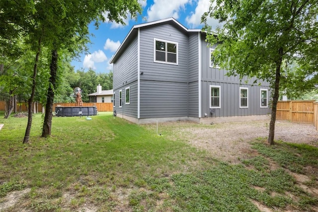 rear view of house with a fenced in pool, a fenced backyard, board and batten siding, and a lawn