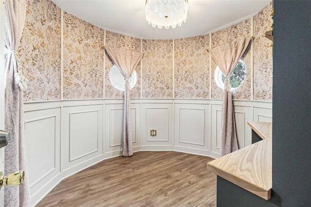unfurnished dining area featuring wallpapered walls, wainscoting, wood finished floors, and a decorative wall