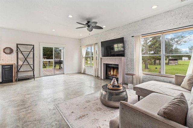 living room with recessed lighting, concrete flooring, a warm lit fireplace, and ceiling fan