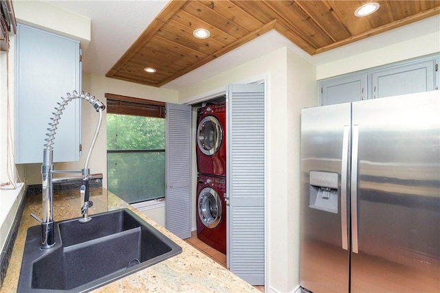 kitchen featuring stainless steel refrigerator with ice dispenser, recessed lighting, wooden ceiling, and stacked washer / dryer
