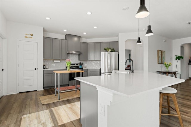 210 Maroon Ln, Kyle, TX 78640 - kitchen featuring appliances with stainless steel finishes, gray cabinetry, under cabinet range hood, arched walkways, and light countertops