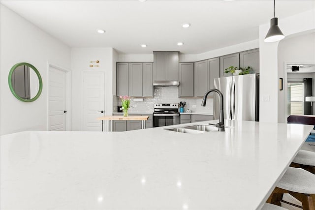 kitchen with a kitchen bar, gray cabinets, a sink, appliances with stainless steel finishes, and backsplash