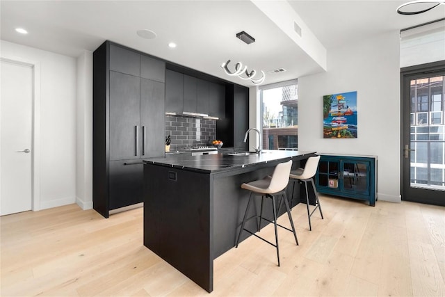 44 E Ave Unit 2907, Austin, TX 78701 - kitchen featuring a kitchen bar, a sink, light wood-type flooring, decorative backsplash, and dark cabinetry