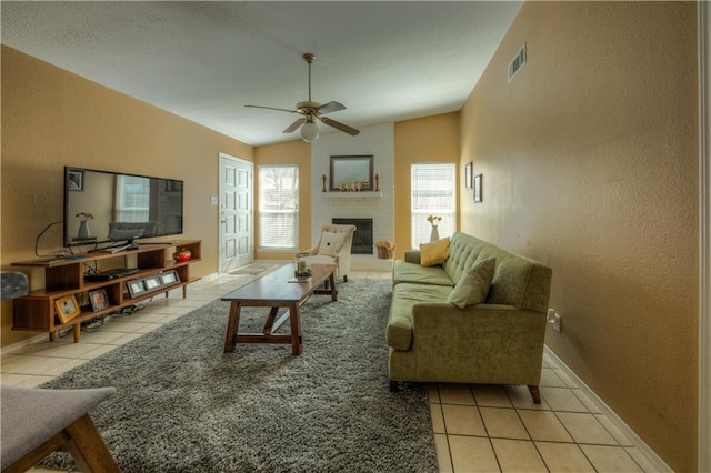 tiled living area featuring a fireplace, a textured wall, a ceiling fan, and visible vents