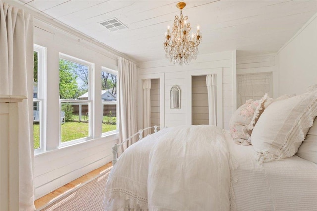 bedroom featuring an inviting chandelier, ornamental molding, visible vents, and wood finished floors