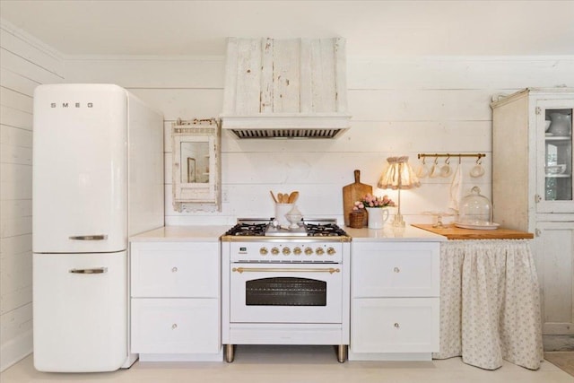 kitchen featuring white cabinets, light countertops, wood walls, and white appliances