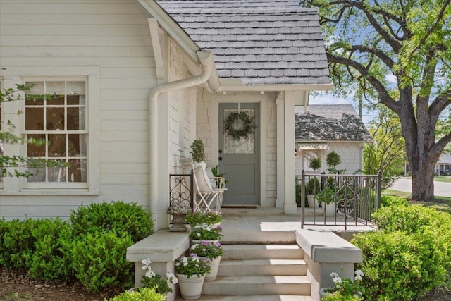 entrance to property with a porch and roof with shingles
