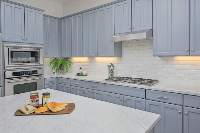 14912 Swallow Tailed Kite Dr, Austin, TX 78738 - kitchen with appliances with stainless steel finishes, under cabinet range hood, decorative backsplash, light stone counters, and gray cabinets