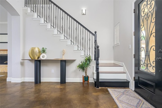 entryway with finished concrete flooring, stairway, baseboards, a towering ceiling, and arched walkways