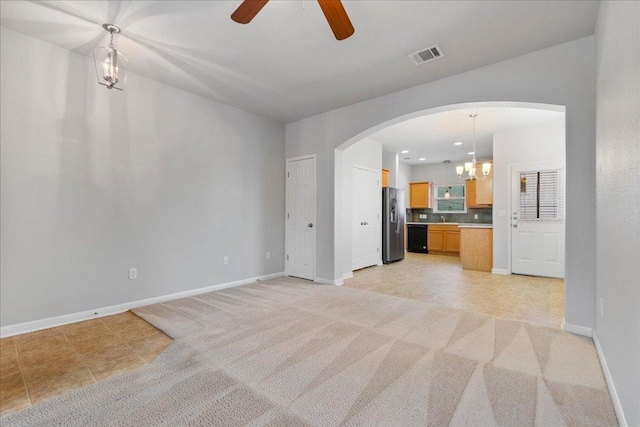 unfurnished living room with arched walkways, a chandelier, a ceiling fan, light colored carpet, and baseboards