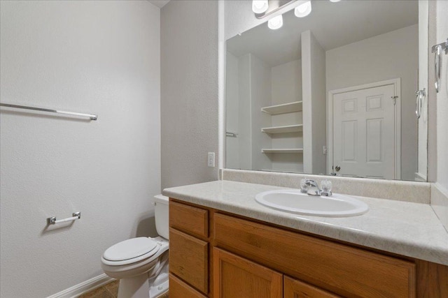 half bathroom with toilet, vanity, baseboards, a textured wall, and tile patterned flooring