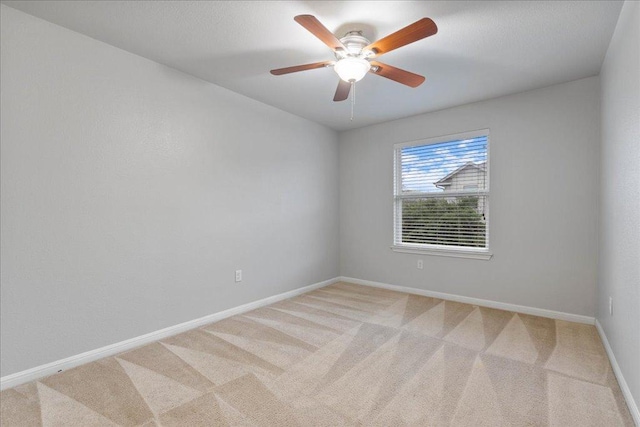 empty room featuring light colored carpet, baseboards, and a ceiling fan