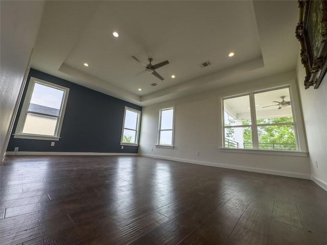 spare room with a tray ceiling, baseboards, a ceiling fan, and dark wood finished floors