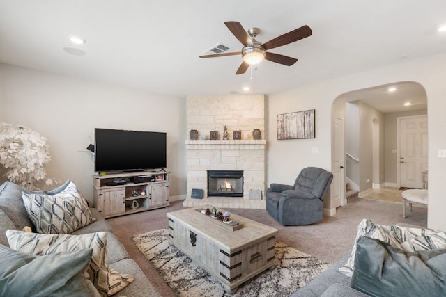130 Mcginnis Trl, Kyle, TX 78640 - carpeted living room with a stone fireplace, ceiling fan, visible vents, arched walkways, and stairway