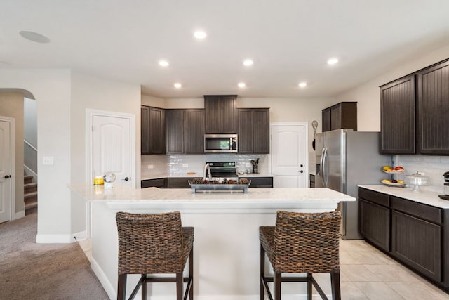 130 Mcginnis Trl, Kyle, TX 78640 - kitchen with stainless steel appliances, tasteful backsplash, a breakfast bar, a kitchen island with sink, and dark brown cabinetry