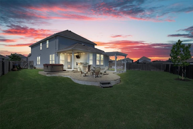 back of property at dusk featuring a yard, a patio, a hot tub, and a fenced backyard