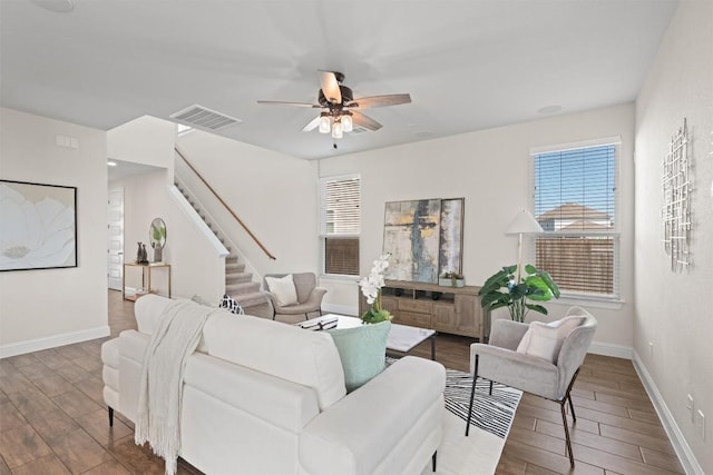 living area featuring a ceiling fan, stairs, visible vents, and wood finished floors