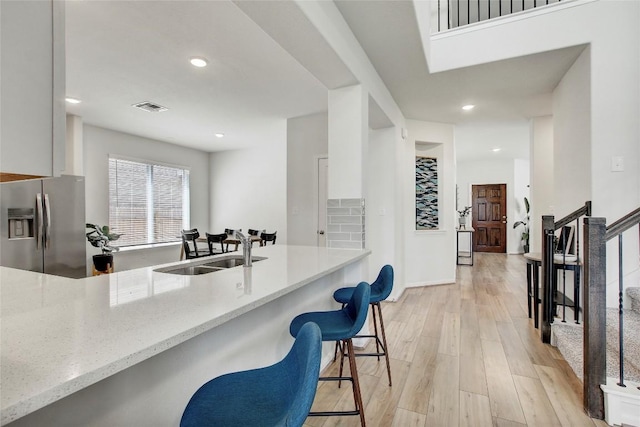 kitchen featuring a sink, light stone counters, visible vents, stainless steel fridge with ice dispenser, and light wood-style floors