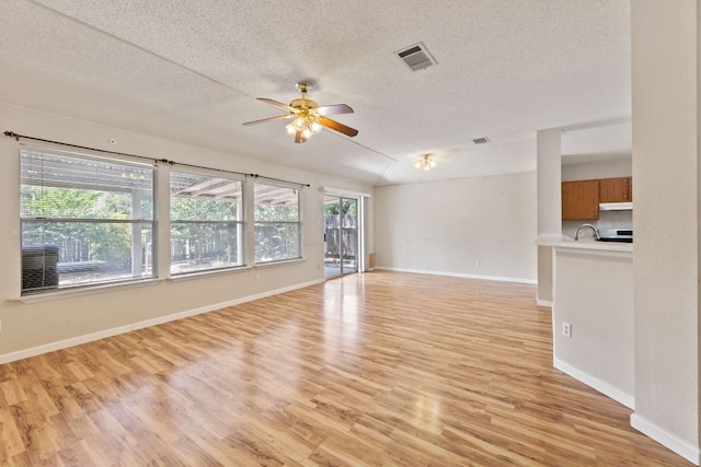 unfurnished living room featuring light wood-type flooring, ceiling fan, a textured ceiling, and baseboards