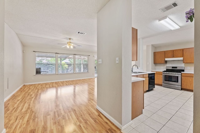 kitchen featuring stainless steel gas stove, black dishwasher, a sink, under cabinet range hood, and a textured ceiling