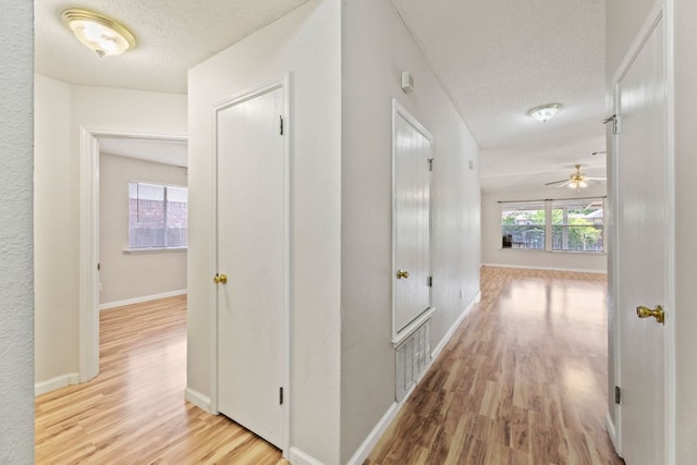 hall featuring wood finished floors, a textured ceiling, and baseboards