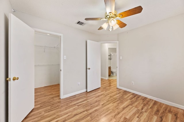 unfurnished bedroom featuring light wood-style flooring, a closet, a spacious closet, and baseboards