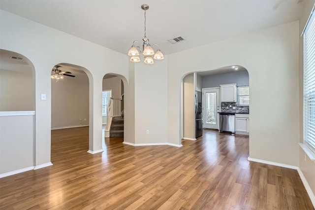 unfurnished dining area featuring light wood-style flooring, baseboards, a healthy amount of sunlight, visible vents, and ceiling fan with notable chandelier
