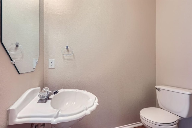half bath with toilet, baseboards, and a sink