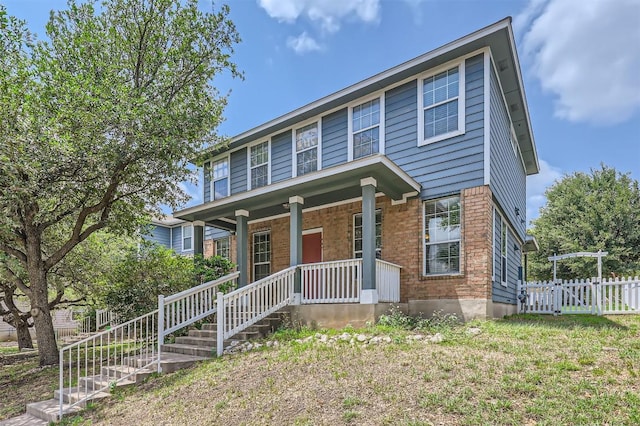 view of front facade featuring a porch, fence, and brick siding